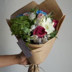 Handheld bouquet with pink roses, white gerbera daisies, and green hydrangea in brown paper