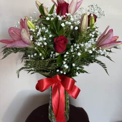 Pink lilies and red roses in a glass vase with a red ribbon