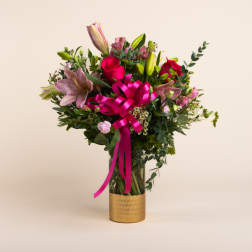 Bouquet of pink lilies and roses in a gold vase with a bright pink ribbon