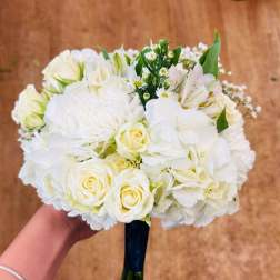 Hand-tied bouquet of white hydrangeas, roses, carnations, and alstroemeria with a dark ribbon-wrapped handle.