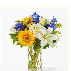 Bouquet of yellow sunflowers, white lilies, and blue flowers in a glass vase