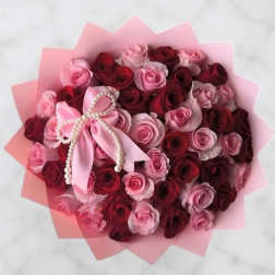Bouquet of pink and red roses with a pink ribbon bow and pearl trim