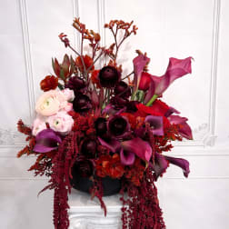 Tall floral arrangement with pink calla lilies, roses, and dark blooms in a black container