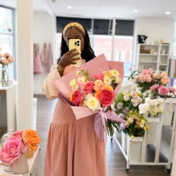Woman holding a pink-wrapped bouquet of multicolored roses