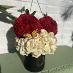 Red carnations and white roses in a black hatbox with butterfly picks