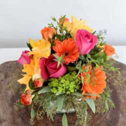 Bright mixed bouquet with pink roses, orange gerberas, and yellow lilies in a low vase