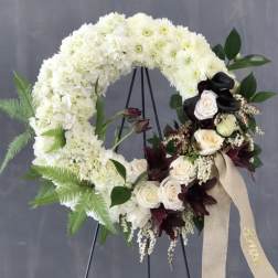White floral wreath on a stand with cream roses and dark accent flowers