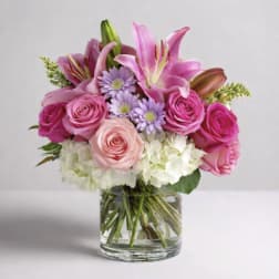 Pink lilies, roses, and lavender daisies in a clear glass vase