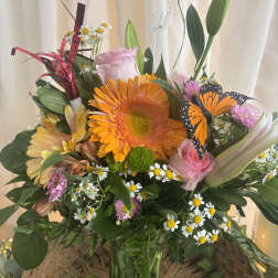 Mixed bouquet with orange gerbera, pink roses, daisies, and a butterfly decoration in a glass vase