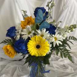 Bouquet of blue roses, white daisies, and yellow gerbera daisies in a glass vase