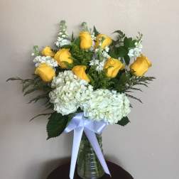 Yellow roses and white hydrangeas in a glass vase with a white ribbon