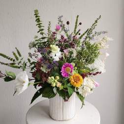 Mixed bouquet in a ribbed white vase with pink, white, yellow, and purple flowers