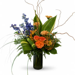 Orange roses and blue flowers in a tall glass vase with curly branches