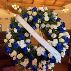 Blue and white floral funeral wreath with a memorial ribbon on an easel