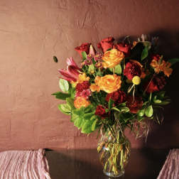 Mixed bouquet of red, orange, and pink flowers in a clear glass vase
