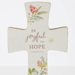 Cross-shaped decorative sign with floral print and the words "Be joyful in hope"