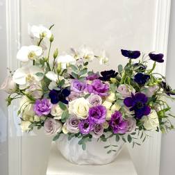 White orchids and purple flowers in a white vase