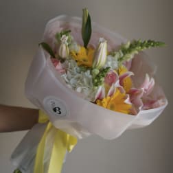 Bouquet of pink and yellow flowers wrapped in pale pink paper with a yellow ribbon