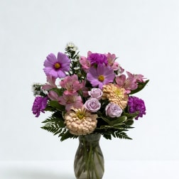 Mixed pink and purple flowers arranged in a glass vase