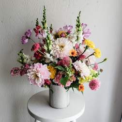 Mixed bouquet of pink, white, yellow, and purple flowers in a ribbed white vase