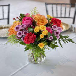 Mixed bouquet of roses, carnations, and purple daisies in a clear glass vase