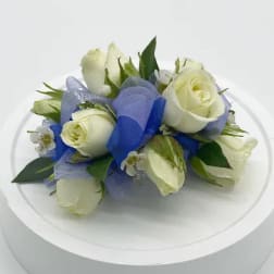 Small cluster of white roses with blue ribbon arranged as a corsage on a white stand