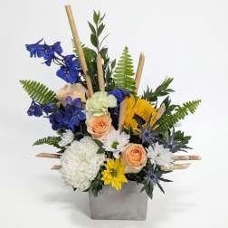 Mixed bouquet in a gray square vase with blue, white, yellow, and peach flowers