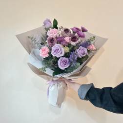 Hand-tied bouquet of lavender roses and pink flowers wrapped in paper
