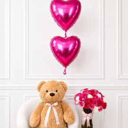 Teddy bear with pink heart balloons and a vase of pink and white roses
