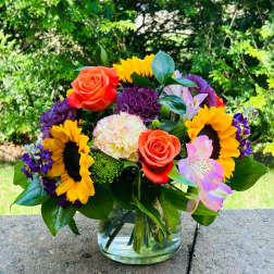 Colorful bouquet with sunflowers, roses, carnations, and alstroemeria in a glass vase