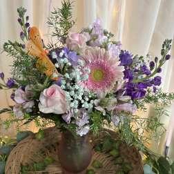 Pink and purple mixed bouquet in a brown vase with an orange butterfly