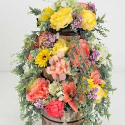 Tiered floral arrangement in a wooden basket with yellow, pink, and coral blooms