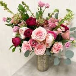 Pink and red rose arrangement with accent blooms in a tall metallic vase on a light surface.