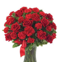 Red roses and carnations in a clear glass vase with a red ribbon