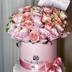 Pink and blush roses arranged in a round pink hat box with a ribbon bow.