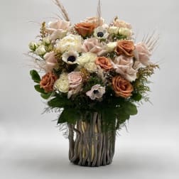 Bouquet of blush and peach roses with white accent flowers in a tall vase