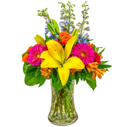 Bright mixed bouquet with yellow lilies, hot pink gerbera daisies and orange roses in a clear glass vase