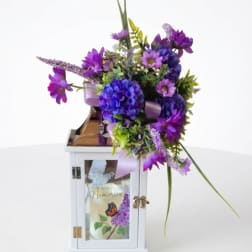 Purple floral arrangement in a white lantern with a candle inside