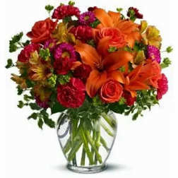 Bouquet of orange lilies, red roses, and mixed flowers in a clear glass vase