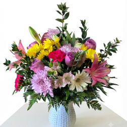 Mixed bouquet of pink, yellow, and lavender flowers in a white vase