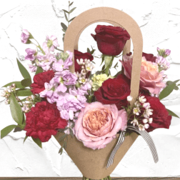 Mixed bouquet of red, pink, and lavender flowers in a kraft paper wrap