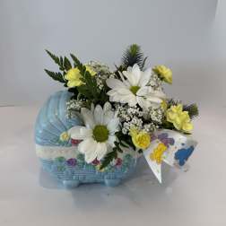 Yellow and white flowers arranged in a blue basket with a teddy bear ribbon