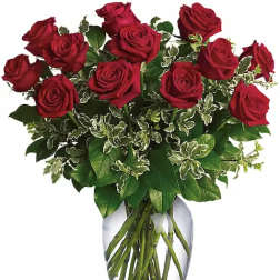 Red roses arranged in a clear glass vase with mixed greenery