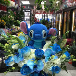 Blue plush character surrounded by blue and white flowers in a round box