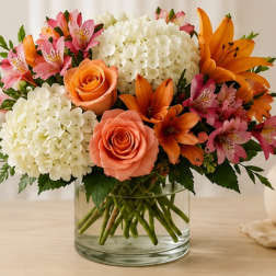 Bouquet of orange roses, lilies, pink alstroemeria, and white hydrangeas in a glass vase