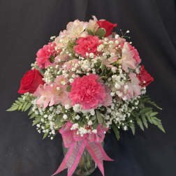 Pink and red flower arrangement in a glass vase with a pink ribbon