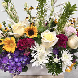 Mixed bouquet with white roses, purple hydrangeas, and yellow daisy-like flowers in a white container.