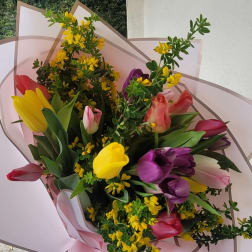 Bouquet of multicolored tulips with yellow filler flowers wrapped in pale pink paper