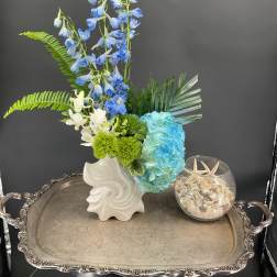Blue and white floral arrangement in a white vase with green accents