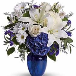 White lilies and daisies arranged in a blue vase with purple accents